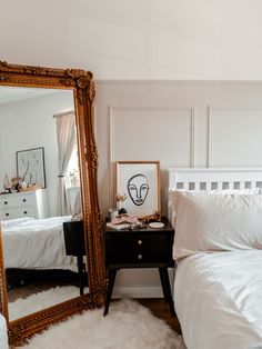 a white bed sitting next to a large mirror on top of a wooden dresser in a bedroom