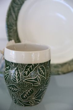 a green and white vase sitting on top of a table next to a plate covered in leaves