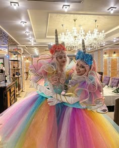 two women dressed as unicorns pose for the camera in front of a chandelier