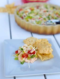 a white plate topped with nachos next to a bowl of salsa and a pizza