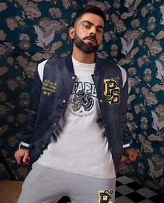 a man standing in front of a wallpapered background wearing a jacket and sweatpants