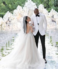 a bride and groom standing in front of an aisle with white flowers on the ground