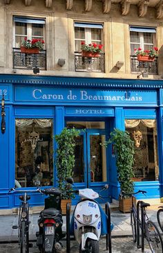 two scooters are parked in front of a blue building with flowers on the balconies