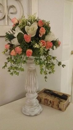 a white vase filled with lots of flowers on top of a table next to a box