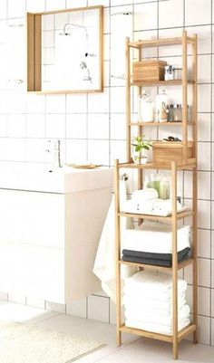 a bathroom with white tiled walls and flooring, including a wooden shelf that holds folded towels