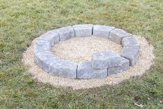 a circular stone fire pit in the middle of some grass with gravel around it and rocks on each side