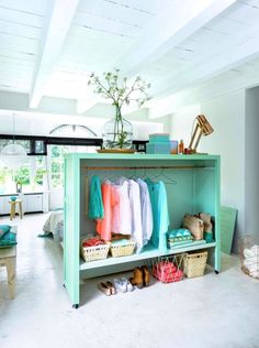 a room filled with lots of clothes and baskets on top of a blue shelf next to a window