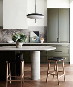 a kitchen with an island and stools in front of the countertop, surrounded by green cabinetry