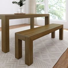 a wooden table and bench in front of a window with white rug on the floor