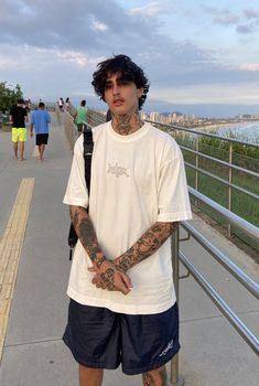 a man with tattoos on his arm standing next to a metal railing near the ocean