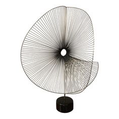 a metal sculpture on top of a black stand next to a white wall in the shape of a fan