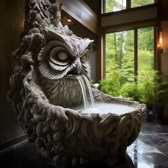 an owl fountain is in the middle of a room with large windows and lots of greenery