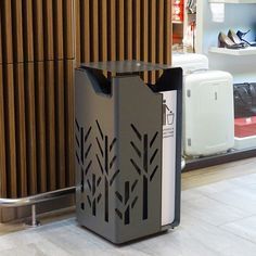 a black trash can sitting on the ground in front of a store window with wooden slats behind it