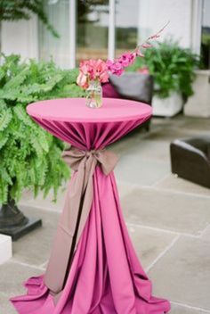 a pink table with a bow on it and flowers in a vase at the top