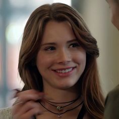 a woman is smiling and adjusting her necklace