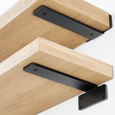 two black brackets are attached to the wall next to a wooden shelf with metal brackets on it