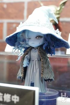 a doll is wearing a white hat with blue feathers on it's brim