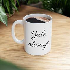 a white coffee mug with the words yule always on it sitting on a wooden table