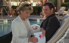 a man and woman sitting next to each other near a swimming pool holding a box