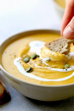 a person dipping some bread into a bowl of pumpkin peanut butter soup with pistachio sprinkles