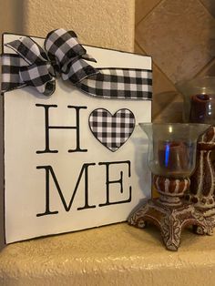 a sign that says home with a candle and vase on the shelf next to it