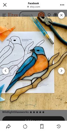 a paper bird sitting on top of a piece of wood next to scissors and pens