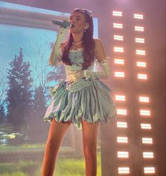 a woman in a green dress holding a microphone on stage with lights behind her and an audience watching