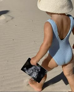 a small child in a blue and white swimsuit is playing with a book on the beach