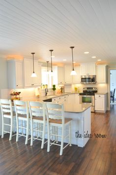 a large kitchen with white cabinets and wooden flooring, along with an island in the middle