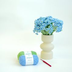 a white vase filled with blue flowers next to a ball of yarn