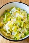 a white bowl filled with salad next to lettuce and lemon wedges on a cutting board