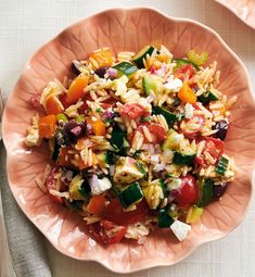 a pink bowl filled with pasta salad on top of a white table next to silverware