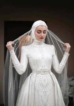 a woman in a white wedding dress with a veil over her head and hands on her hips