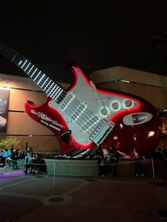 a giant guitar sculpture in front of a building with people standing around it at night