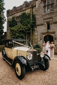 a bride and her bridal party standing in front of an old car outside the castle