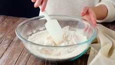 a woman mixing ingredients in a bowl on top of a wooden table with a white spatula