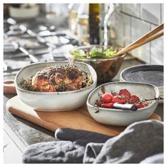 two bowls filled with food sitting on top of a wooden cutting board next to an oven