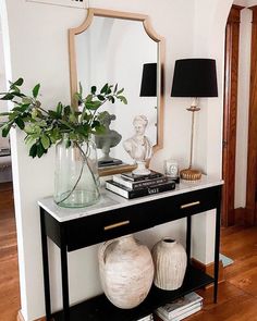 a table with two vases and a mirror on top of it next to a lamp