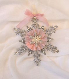 a snowflake is laying on a white sheet with pink ribbon and bow around it