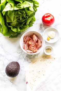 ingredients to make an avocado salad laid out on a marble counter top with lettuce, tomatoes and other vegetables