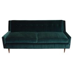 a green velvet couch with wooden legs