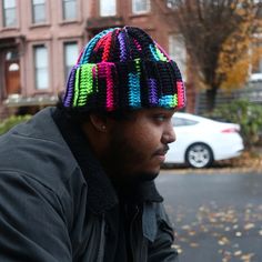 a man wearing a multicolored knitted hat sitting on the side of a road