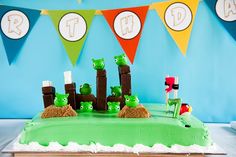 a green cake with angry birds on it and bunting flags in the background that say happy birthday