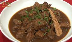 a white bowl filled with meat and gravy on top of a red table