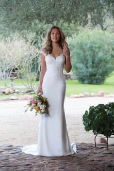 a woman in a white wedding dress holding a bouquet and looking at the camera with her hand on her hip