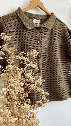 a close up of a sweater on a hanger next to some dried plants and flowers