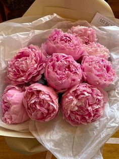 a bunch of pink peonies sitting on top of a white table cloth in a bowl