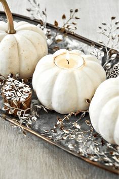 some white pumpkins are sitting on a tray with silver florets and leaves