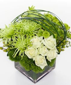 a vase filled with white flowers and greenery on top of a glass block table