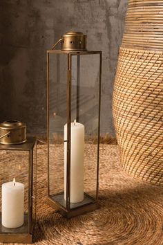 two white candles sitting next to each other on top of a table with a basket in the background